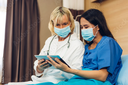 Senior woman doctor wearing protective mask with stethoscope service help support discussing and consulting talk to sick woman patient about checkup result information with tablet in hospital