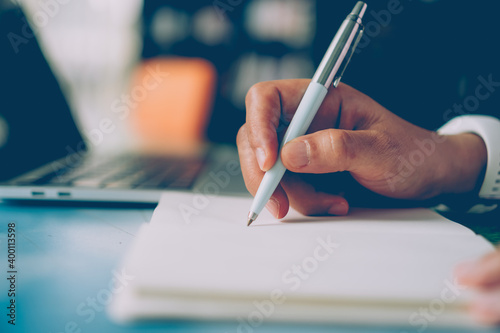 Woman hand writing down in small white memo notebook for take a note not to forget or to do list.