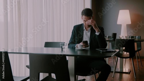Businessman sitting at an empty table and typing on his phone with a concern face