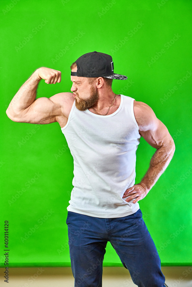 Fototapeta premium sports caucasian shows biceps muscles in a t-shirt and cap on a green background. The man smiles. High quality photo