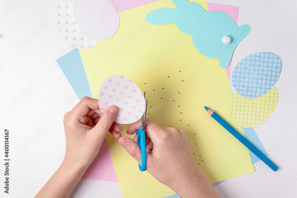 Caucasian boy cutting out Easter egg with scissors. Colored cardboard, paper, pencils. Easter dotted eggs. Top view. Easter indoors activity games. Dot to dot rabbit. Top view. Caucasian boy cutting out Easter egg with scissors. Colored cardboard, paper, pencils. Easter dotted eggs. Top view. Easter indoors activity games. Dot to dot rabbit. Top view.