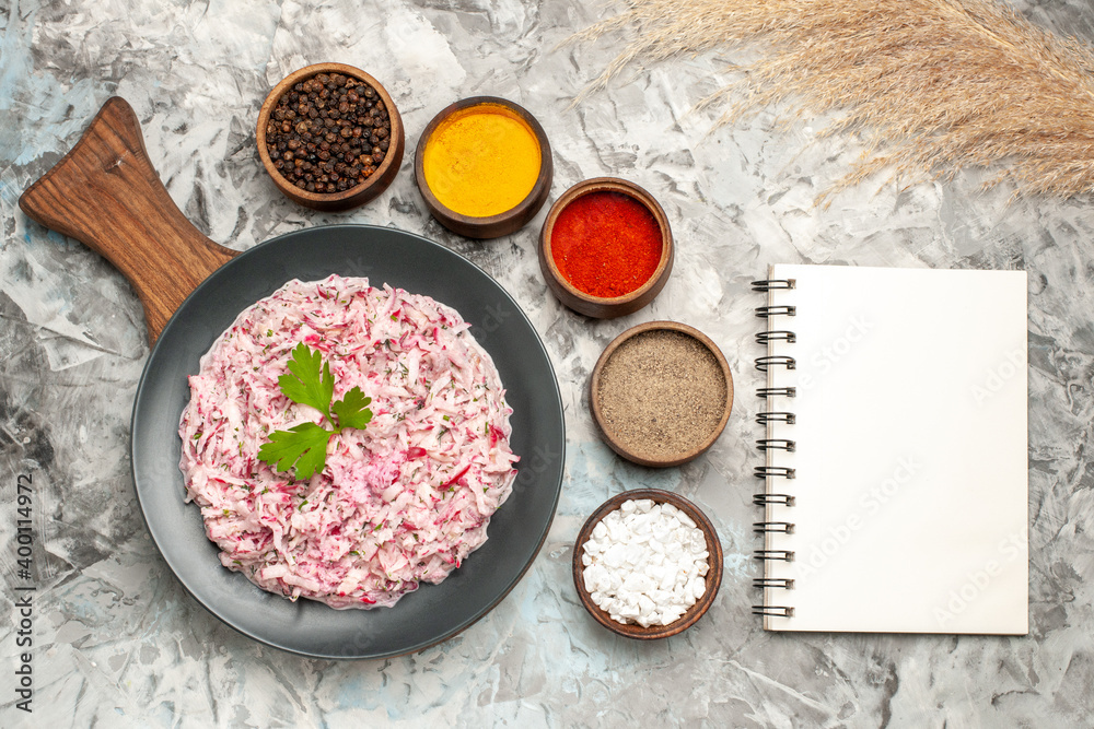 Overhead view of tasty chicken salad with mayonnaise and beet served with green on brown wooden cutting board and different spices next to notebook Overhead view of tasty chicken salad with mayonnaise and beet served with green on brown wooden cutting board and different spices next to notebook