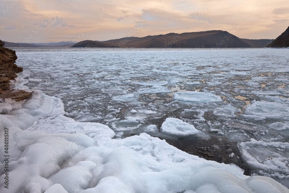 Baikal Lake in December sunrise. View on Olkhon Gate Strait at freeze-up time. Floating ice floes near coast and open water in the strait. Beautiful winter landscape. Natural background. Winter travel