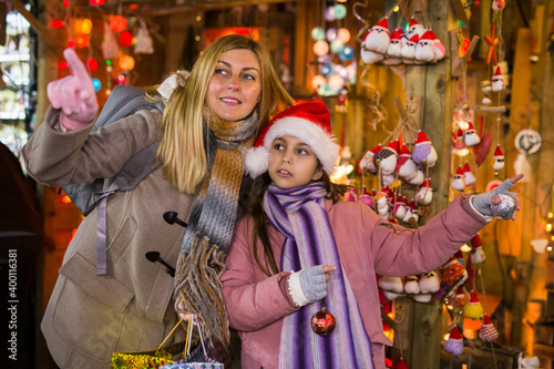 Happy daughter with mom point finger at selected christmas tree decorations at street christmas market