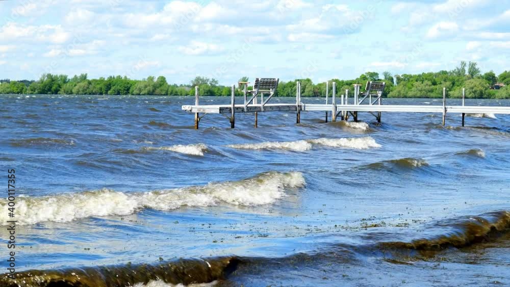 Boat dock with empty benches on a lake in northern Minnesota, with white waves rolling onto the beach on a windy day with partly cloudy sky. Slow motion. Boat dock with empty benches on a lake in northern Minnesota, with white waves rolling onto the beach on a windy day with partly cloudy sky. Slow motion.