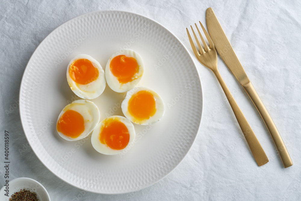 Soft-boiled eggs, peeled and cut into two halves, lying on white plate. High cholesterol, healthy Breakfast, protein food. Soft-boiled eggs, peeled and cut into two halves, lying on white plate. High cholesterol, healthy Breakfast, protein food.