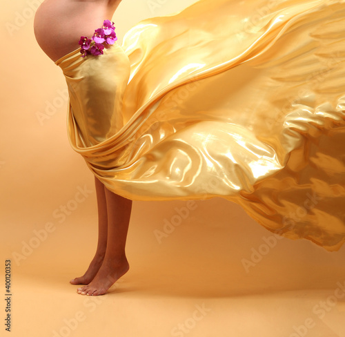 Pregnant woman with Orchid flowers and gold fabric on yellow background