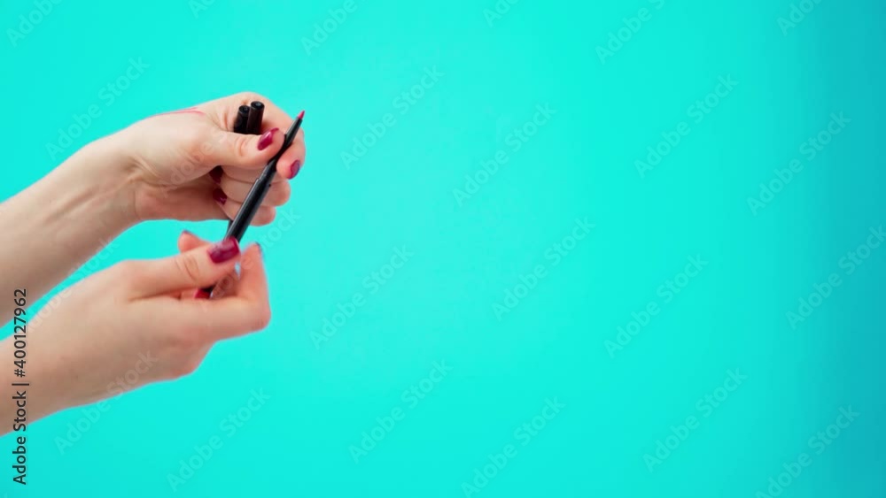 Female hands holding cosmetic eye liner pencils against blue background Female hands holding cosmetic eye liner pencils against blue background