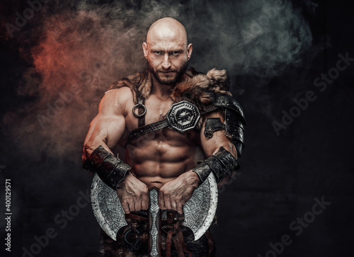Powerful and shirtless viking warrior with bald head dressed in steel lights armour with fur poses in dark atmospheric background