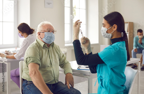 Senior patient waiting to get a shot and looking at young doctor getting the vaccine ready photo