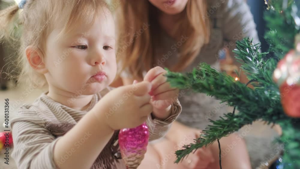 Baby decorates Christmas tree. Toddler girl decorates the Christmas pine tree with her family Baby decorates Christmas tree. Toddler girl decorates the Christmas pine tree with her family