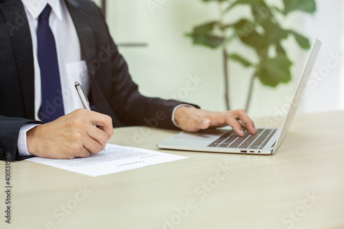 Close up hand of businessman holding pen and writting on paperwork using laptop in office. business concept.