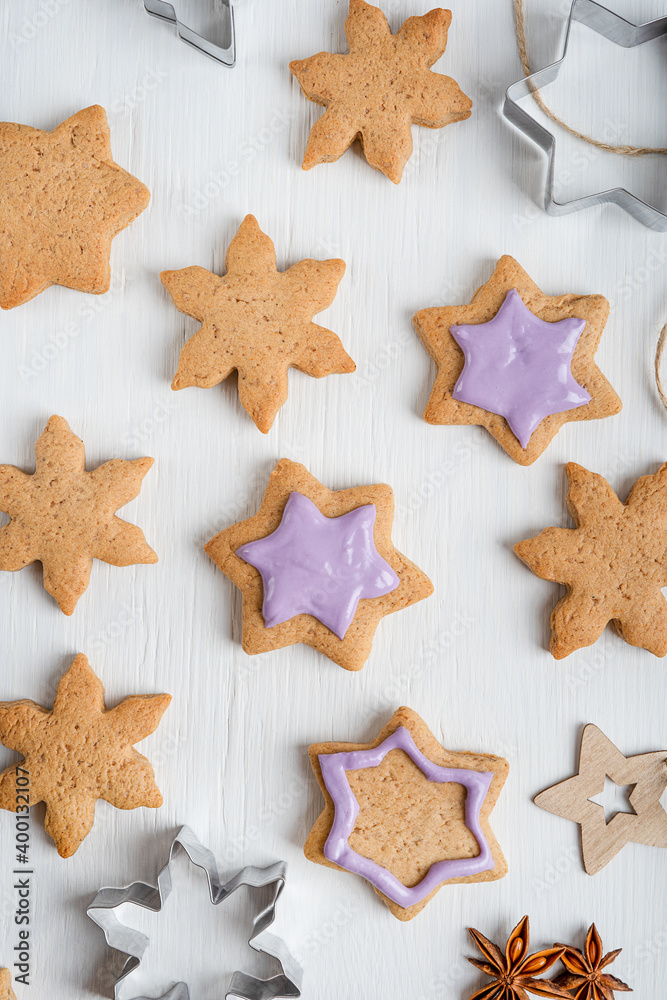 Pattern made of sweet savory ginger cookies or gingerbread with violet icing decoration and cutters cooked for christmas holidays at winter laying on white wooden table at kitchen. Vertical Pattern made of sweet savory ginger cookies or gingerbread with violet icing decoration and cutters cooked for christmas holidays at winter laying on white wooden table at kitchen. Vertical