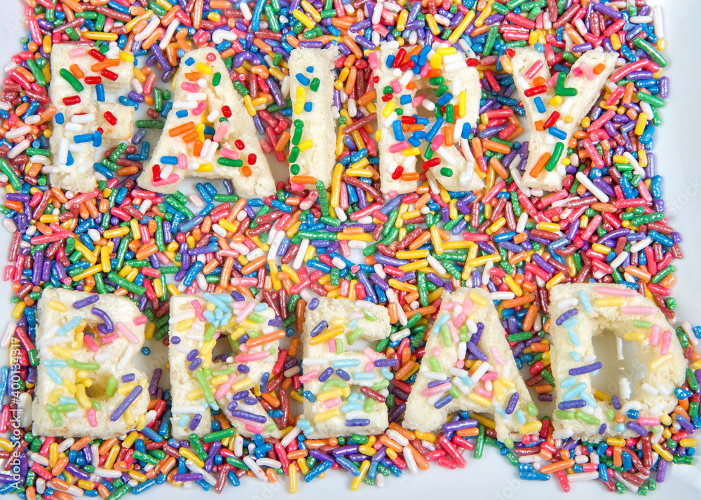 Fairy bread spelled with fairy bread on rectangular plate, with candy sprinkles spilled about. Fairy bread is commonly served at children's parties in Australia and New Zealand.