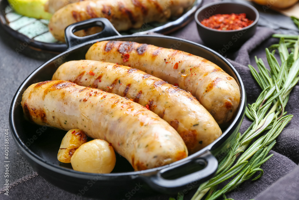 Pan with delicious grilled sausages and spices on dark background Pan with delicious grilled sausages and spices on dark background