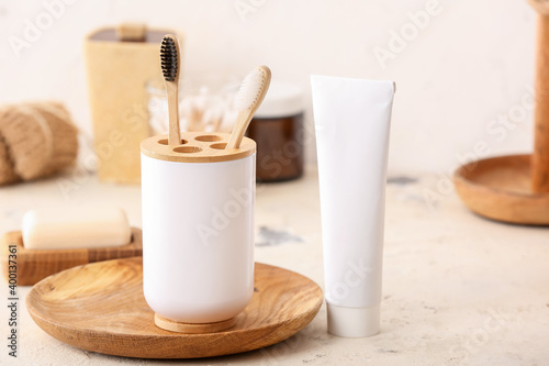 Holder with wooden toothbrushes and toothpaste on table in bathroom