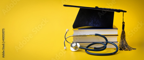 medical education - college graduation cap with stethoscope and books on yellow background with copy space