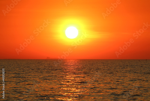 Bright sun on the vivid orange sky setting over the calm sea