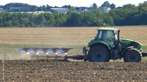 Farmer Ploughing Soil using Tractor with Mouldboard Plough on Sunny Day photo