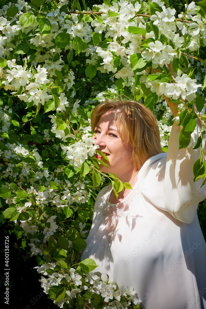 Outdoor portrait of a beautiful blonde middle-aged woman near blossom apple trees with white flowers. Outdoor portrait of a beautiful blonde middle-aged woman near blossom apple trees with white flowers.