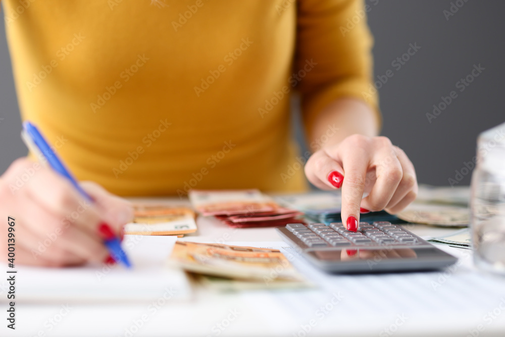 Woman is counting on calculator and writing with pen in notebook closeup