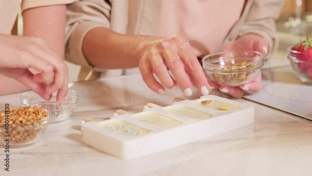 No face close up of unrecognizable female hands decorating homemade ice-cream in forms with nuts before freezing No face close up of unrecognizable female hands decorating homemade ice-cream in forms with nuts before freezing