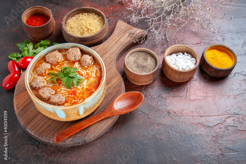 Side view of tomato meatballs soup with noodles in a brown bowl and different spices oil bottle onion garlic on dark background image