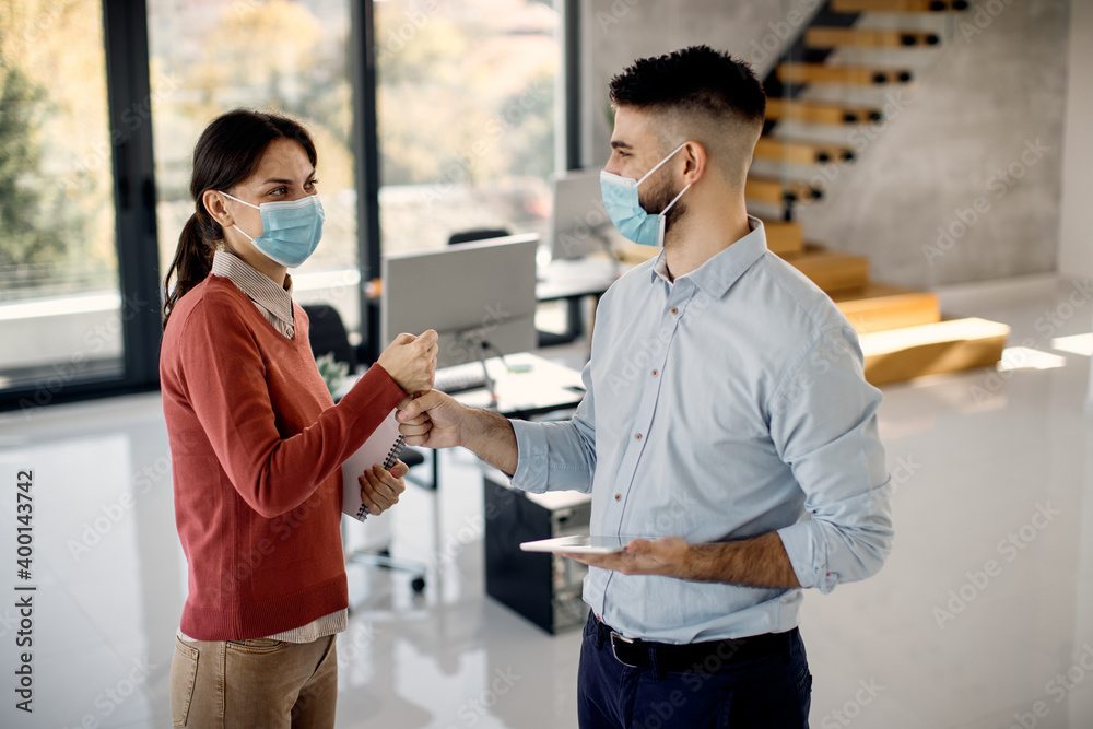 Happy business colleagues wearing face masks while greeting with fists in the office. Happy business colleagues wearing face masks while greeting with fists in the office.