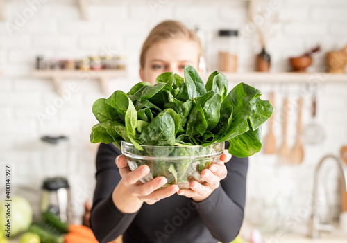 Tableau sur toile Young blond smiling woman holding a bowl of fresh spinach in the kitchen