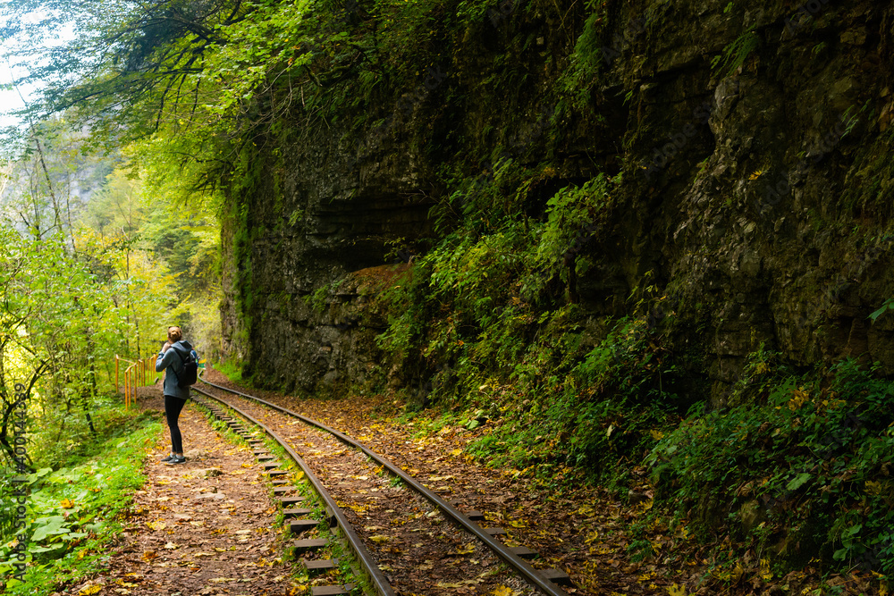 Fototapeta premium Rear view of a young hiking tourist girl enjoying amazing beauty of nature. Excursion on old narrow railroad in mountain region