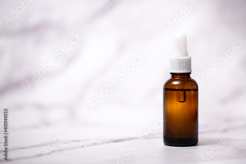 A bottle of cosmetic oil for skin care on a light marble background. Falling drop of oil from a pipette close-up. Beneficial enzymes and vitamins of squalene, flower water and beauty serum.