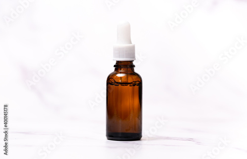 A bottle of cosmetic oil for skin care on a light marble background. Falling drop of oil from a pipette close-up. Beneficial enzymes and vitamins of squalene, flower water and beauty serum.
