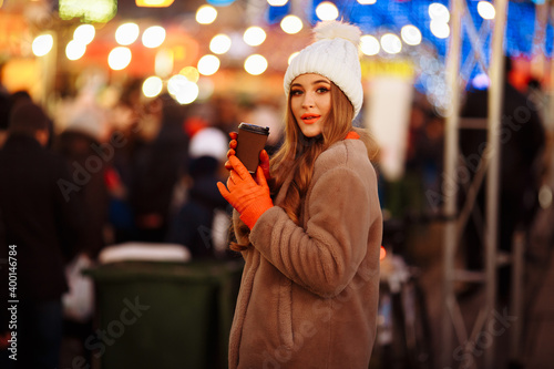 beautiful girl on the background of lights with coffee, on the street, holiday, new year. a walk through the evening city smiles