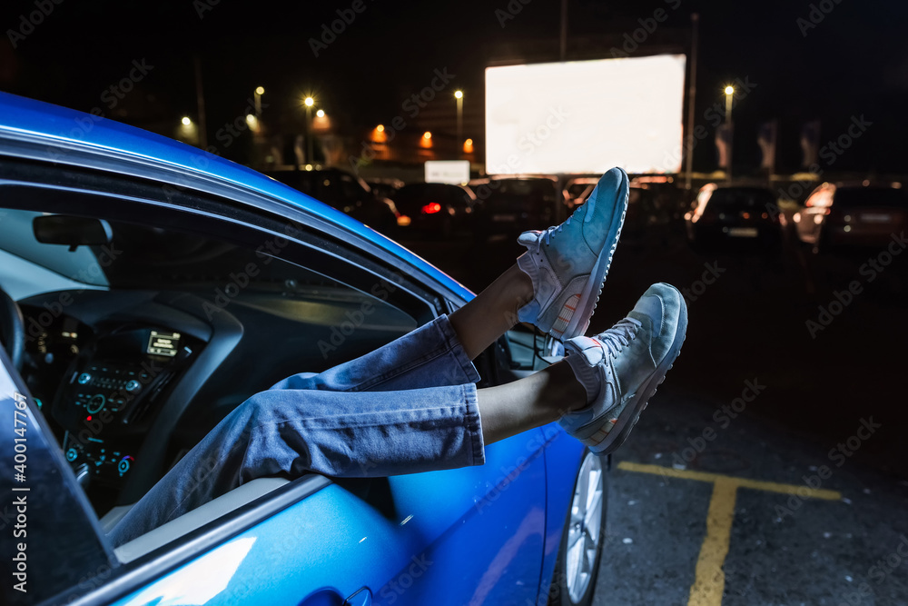 Close up of woman hanging her legs out of car window while watching a movie at drive in cinema from the front seat of the car