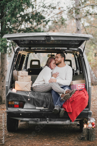 Happy young couple in love sitting in a van decorated with festive Christmas lights, hugging and laughing. © polinaloves