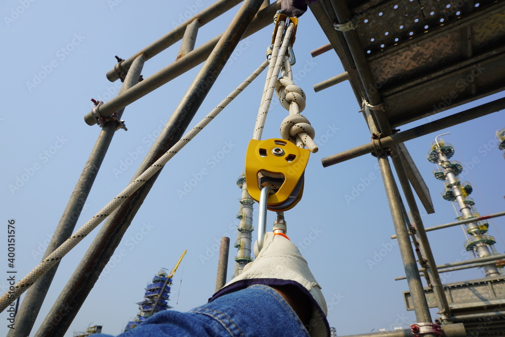 The male hand of rope access industry worker attaching, tie, secure a White rope with figure of eight knot into Aluminum safety harness loop equipment and pulley.