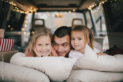 Happy father and his kids having fun in a van decorated with festive Christmas lights.