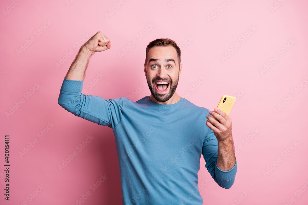 Photo of lucky young guy wear blue pullover holding modern gadget rising fist isolated pink color background Photo of lucky young guy wear blue pullover holding modern gadget rising fist isolated pink color background