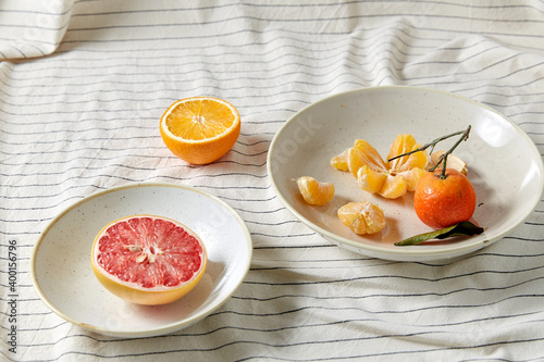 food, healthy eating and fruits concept - close up of mandarin, grapefruit and orange on plates over drapery