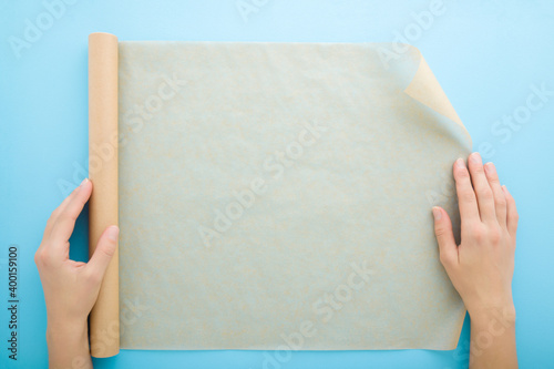 Young adult woman hands using roll of baking paper on light blue table background. Pastel color. Closeup. Point of view shot. Top down view.