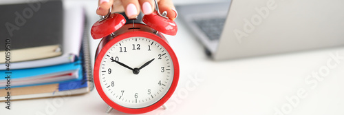 Woman's hand lies on red alarm clock notebooks and laptop lie next to it. How to deal with stress when there is deadline concept at work