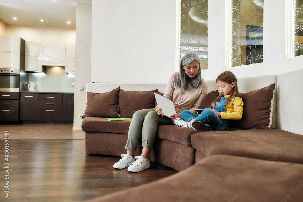 Little girl playing on tablet while sitting beside grandmother