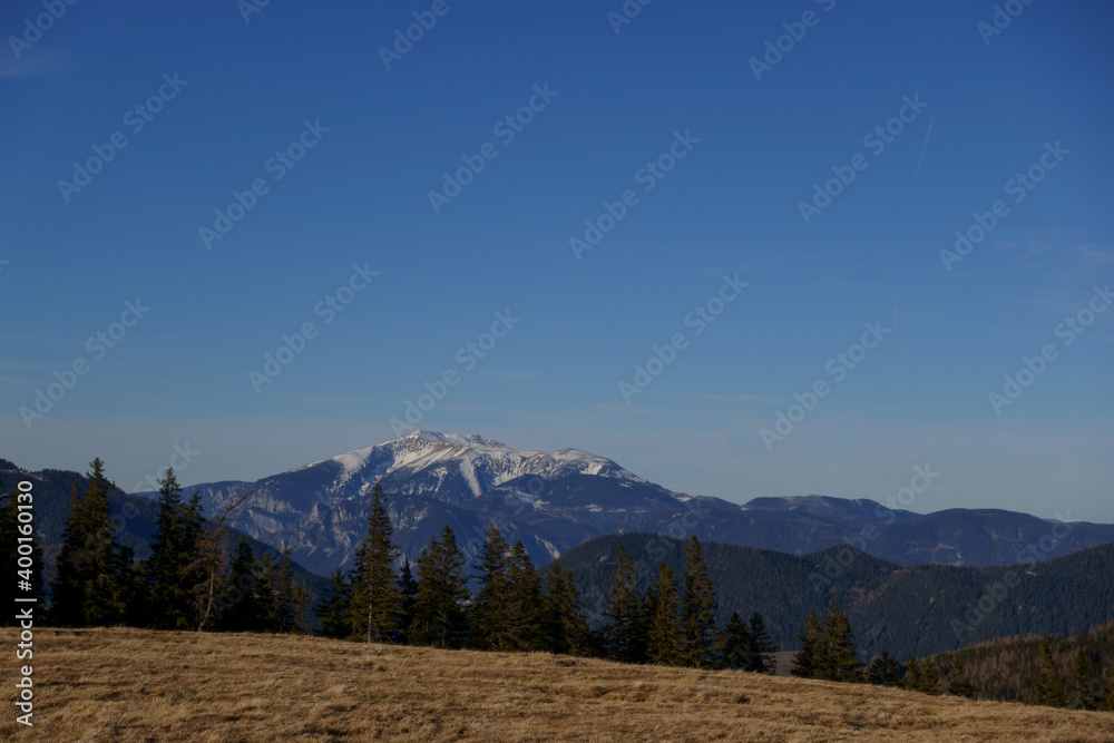 view to a hill with grass and high mountain with snow