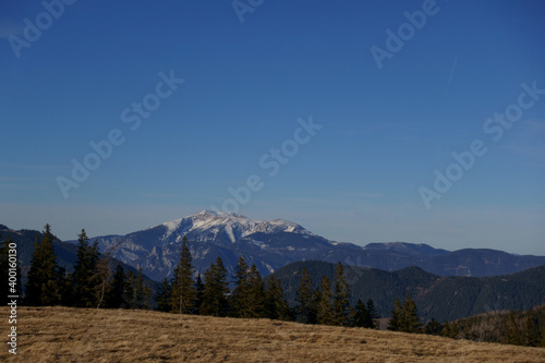 view to a hill with grass and high mountain with snow