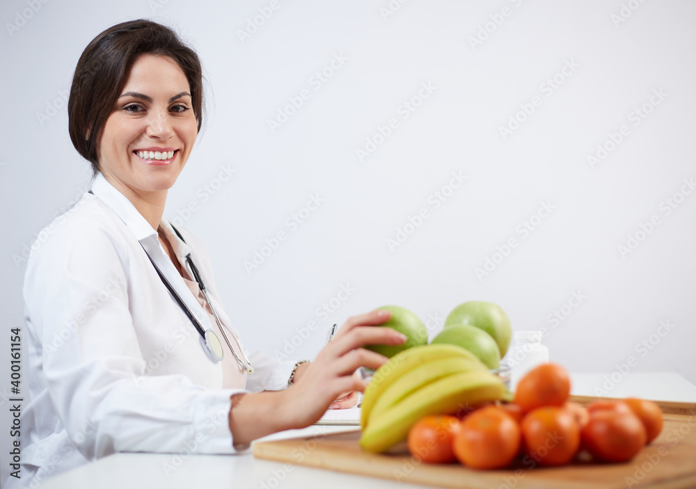 Beautiful smiling nutritionist looking at camera and showing healthy fruits Beautiful smiling nutritionist looking at camera and showing healthy fruits