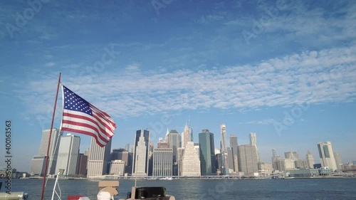 American flag waving in the wind with the iconic New York City Lower Manhattan skyline in the background. Filmed from Brooklyn Bridge Park.