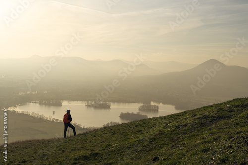 Male hiker looking at rolling landscape and hills of Czech Central Mountains at sunset photo