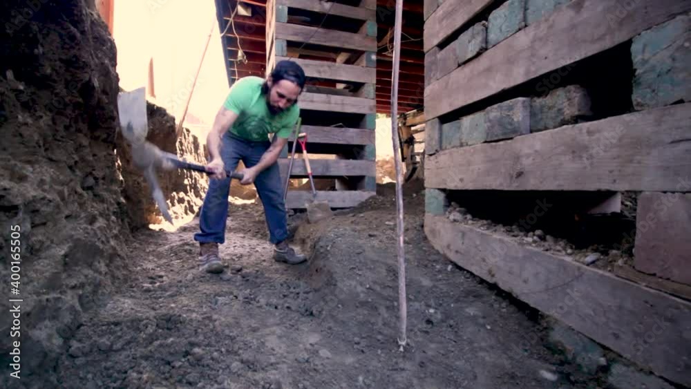Man Digging Foundation At The Construction Site With A Pickaxe - tilt-up shot Man Digging Foundation At The Construction Site With A Pickaxe - tilt-up shot