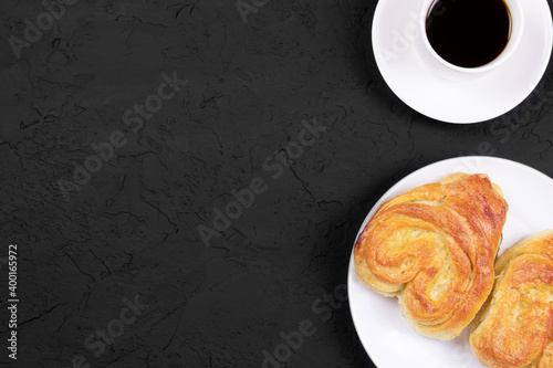 Pastry on a white plate and cup of coffee on a black background. Homemade cake. Fresh baked cake. Breakfast. White cup of coffee on a stone background. Flat lay. Copy space. Place for text.