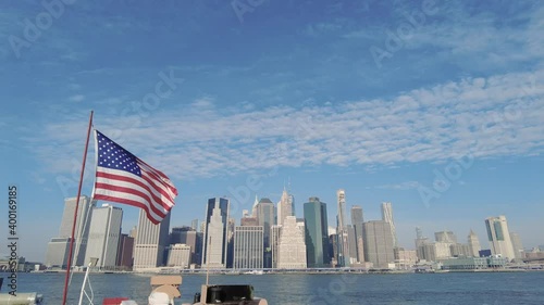 New York City skyline with a number of iconic skyscraper buildings with an American flag waving in the foreground.